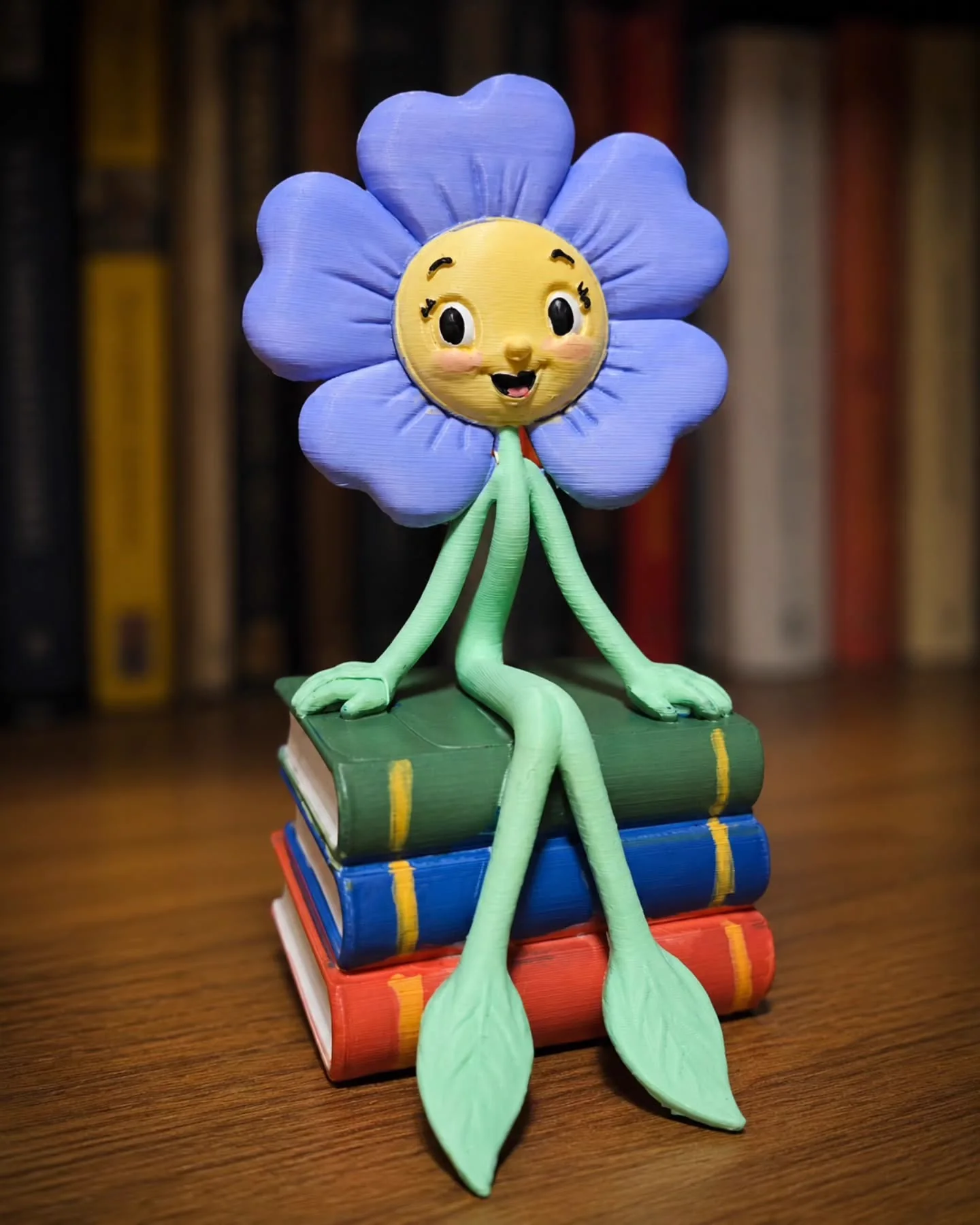 Mascote em forma de flor roxa sentada sobre livros coloridos